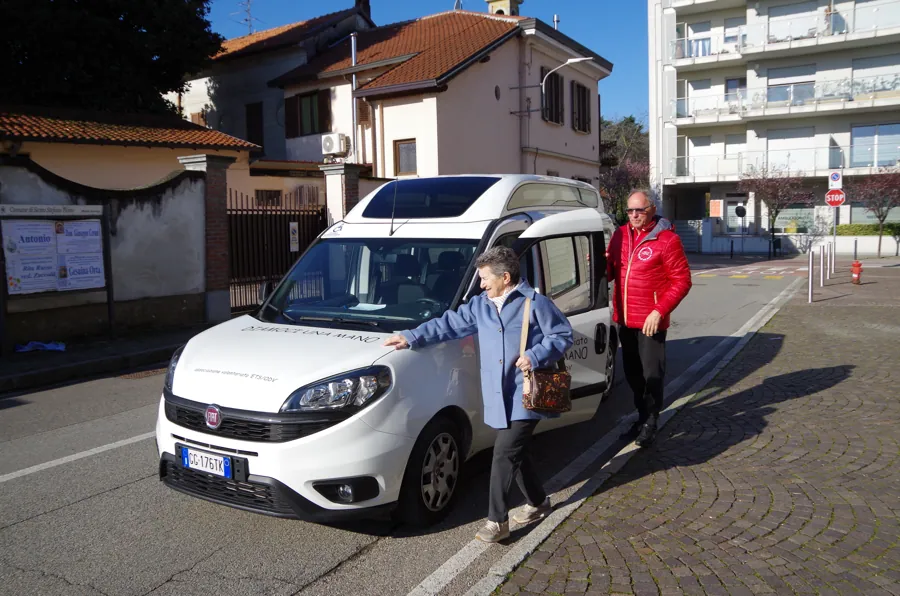 Una volontaria accompagna una signora verso l’auto dell’associazione